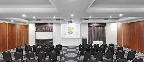 A conference room with rows of chairs, a podium, and a projector screen.