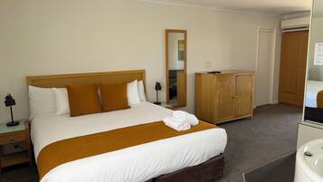 A hotel room with a large bed, wooden headboard, a wardrobe, a mirror, and a bathroom with a sink and toilet.