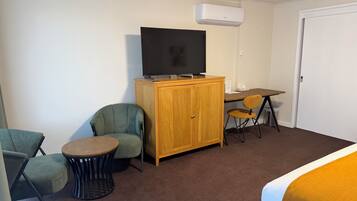 A hotel room with a wooden cabinet, a television, a desk, two chairs, and a bed.