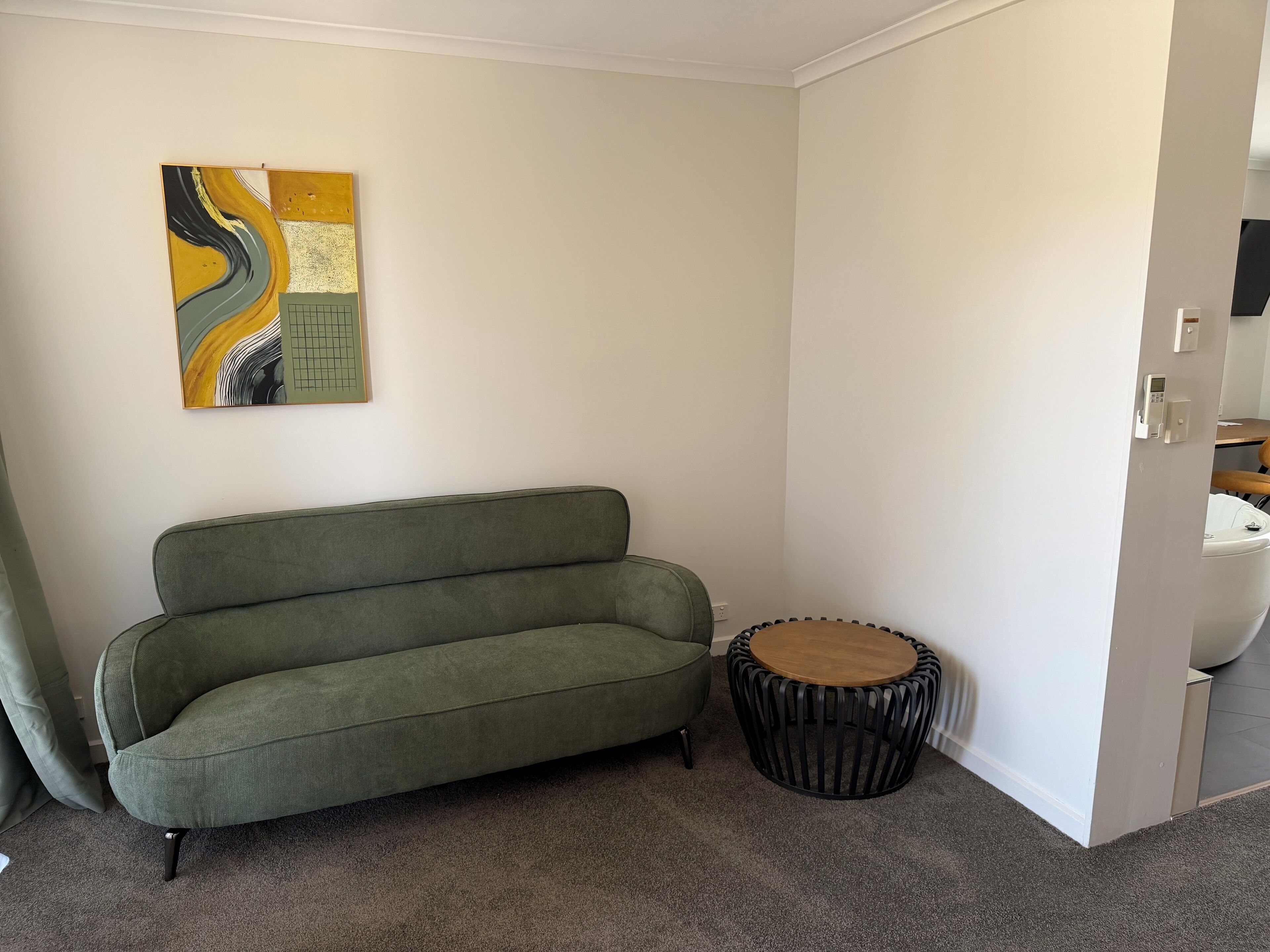 Ein Zimmer mit einem grünen Sofa, einem runden Holztisch und einem an der Wand hängenden abstrakten Gemälde.
