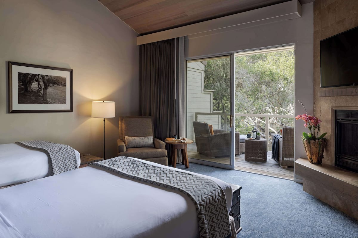 A hotel room with two beds, a sofa, a TV, a fireplace, and a balcony with outdoor furniture.