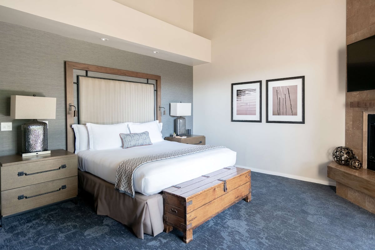 A modern hotel room with a large bed, wooden nightstands, a flat-screen TV, and two framed artworks on the wall.