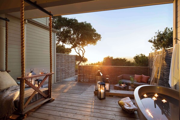 A wooden deck with a swing, a seating area with cushions, and a hot tub.