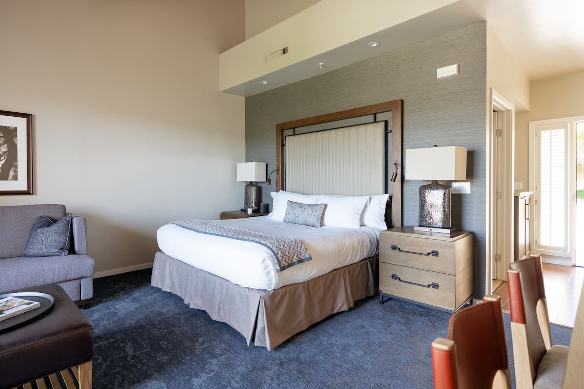 A hotel room with a large bed, a bedside table with a lamp, a sofa, and a small table with a magazine.