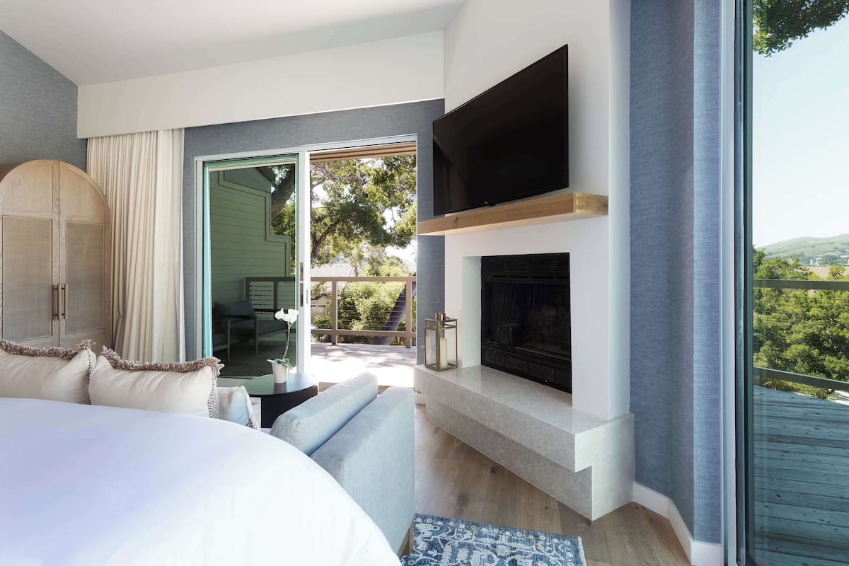 A modern bedroom with a large bed, a fireplace, and a TV mounted above it.