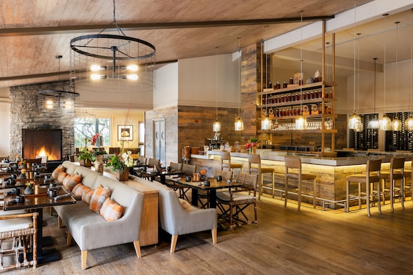 A spacious lounge area with a long sofa, multiple tables, and a bar area with stools.