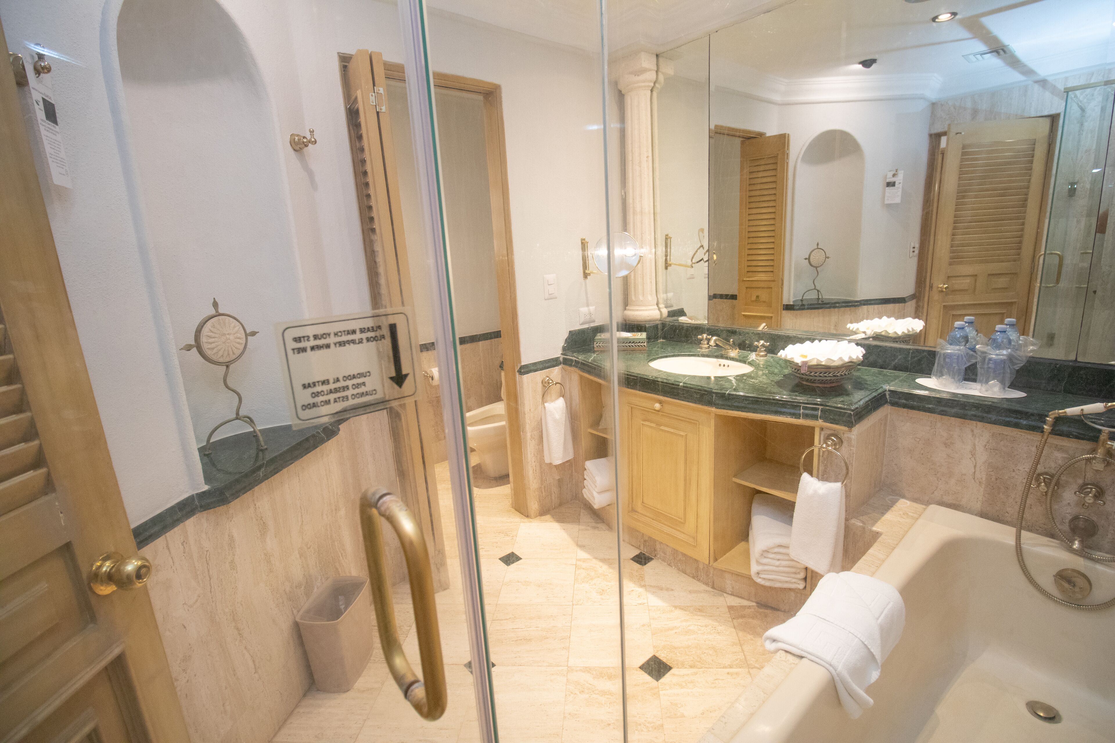 A bathroom with a glass shower enclosure, a bathtub, a sink with a marble countertop, and wooden cabinets.