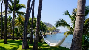 Un'amaca legata tra palme che si affaccia su una distesa d'acqua calma con un'isola in lontananza.