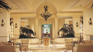 Un'ampia hall con un grande lampadario, due divani, un tavolino da caffè e piante decorative.