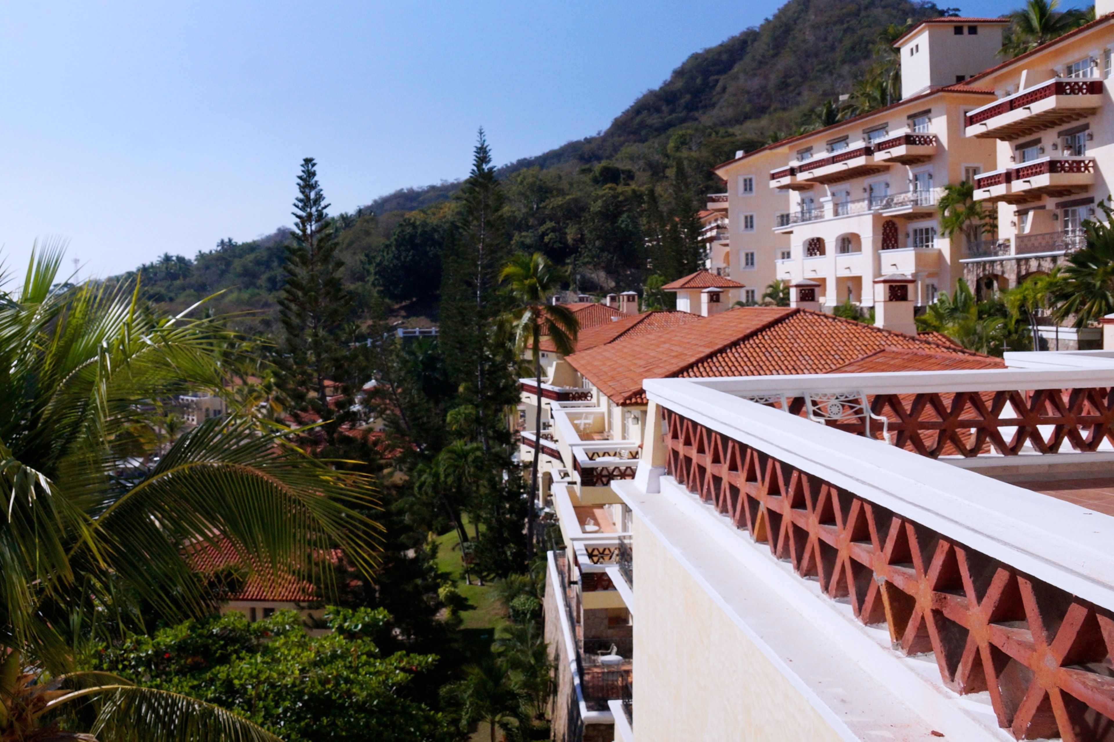 Ein Hotel mit mehreren Balkonen, einem Bergpanorama und üppiger Vegetation.