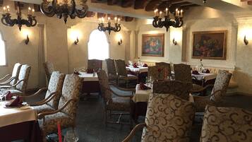 Un restaurante con varias mesas, candelabros ornamentados, sillas estampadas y pinturas clásicas en las paredes.