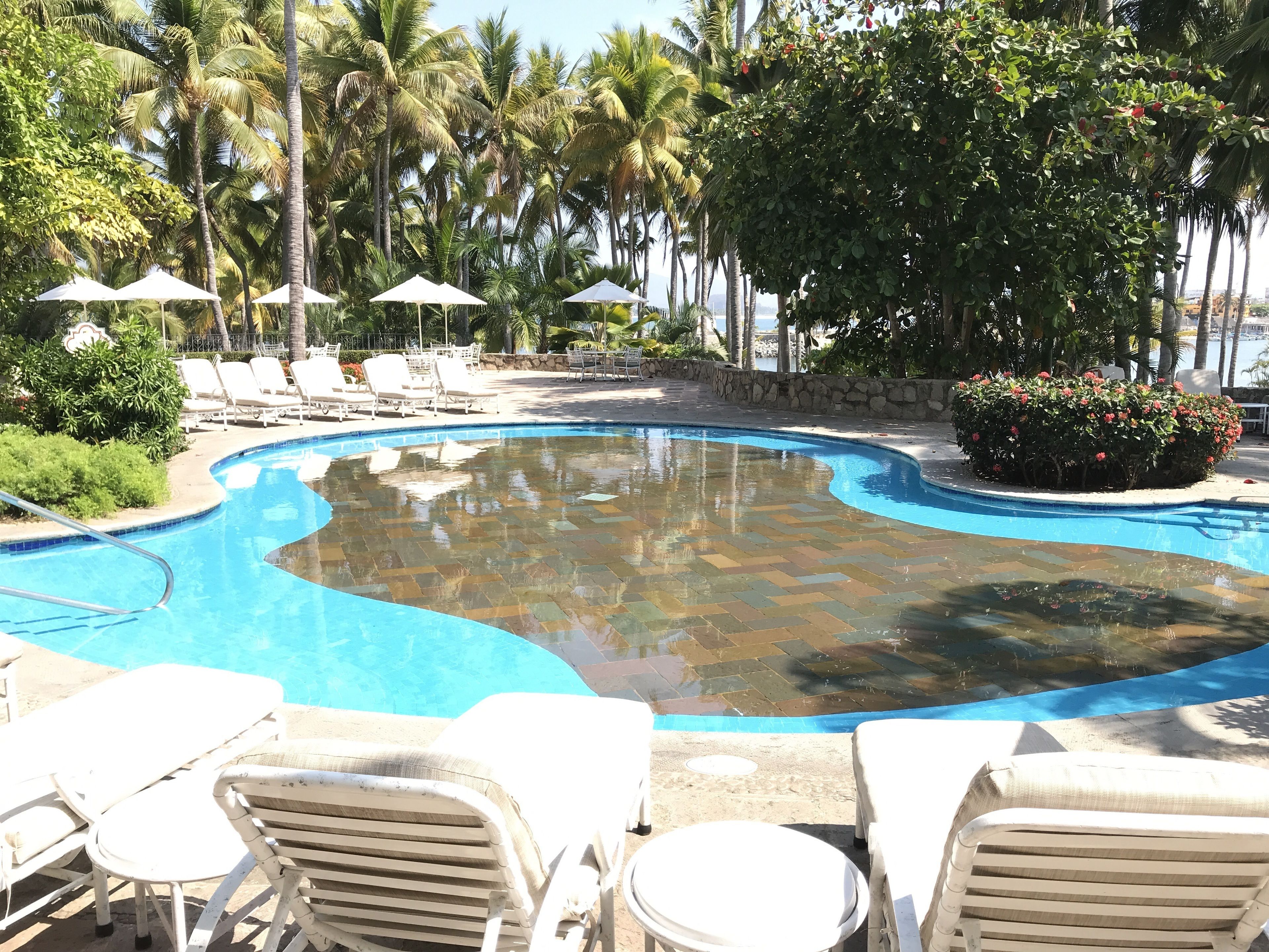 A swimming pool with a curved edge, surrounded by lounge chairs and umbrellas.