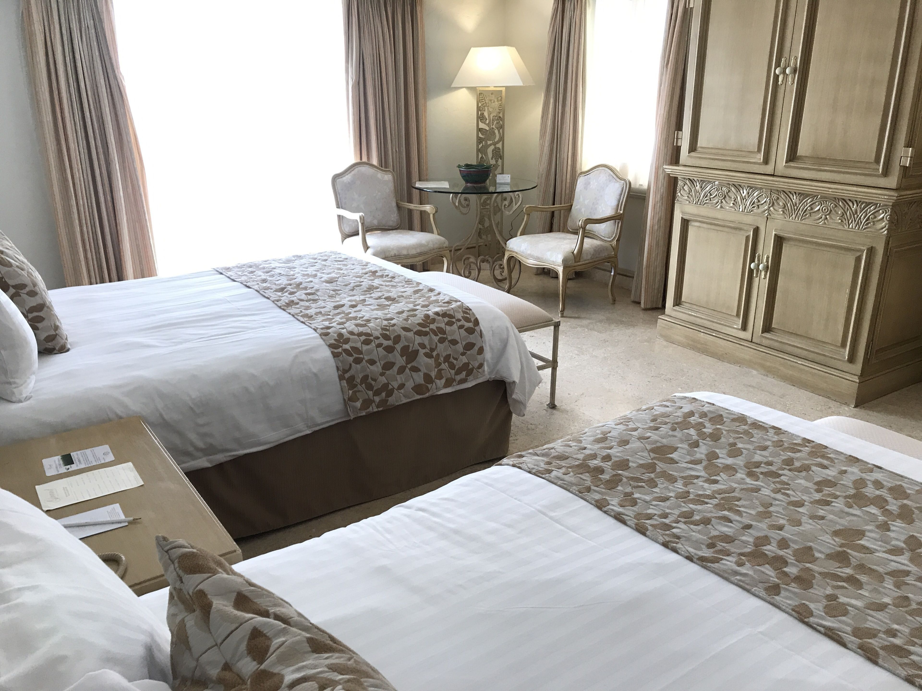 Habitación de hotel con dos camas, un escritorio, sillas y un armario.