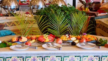 Ein Buffet mit verschiedenen Früchten und Gemüse, darunter Bananen, Äpfel und Orangen, präsentiert auf einer gefliesten Theke mit dekorativen Kacheln.
