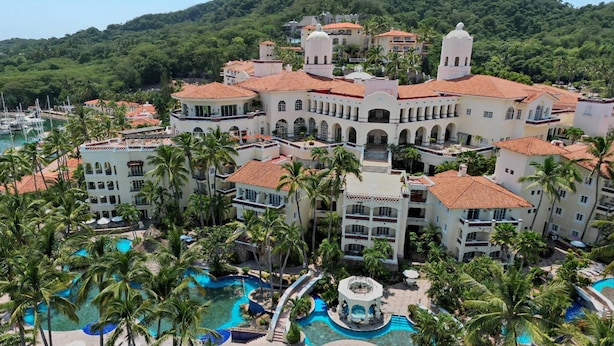 Un resort con diversi edifici, un cortile centrale e una grande piscina circondata da palme.
