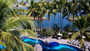 Piscina di un resort con palme, sdraio e vista sull'oceano.