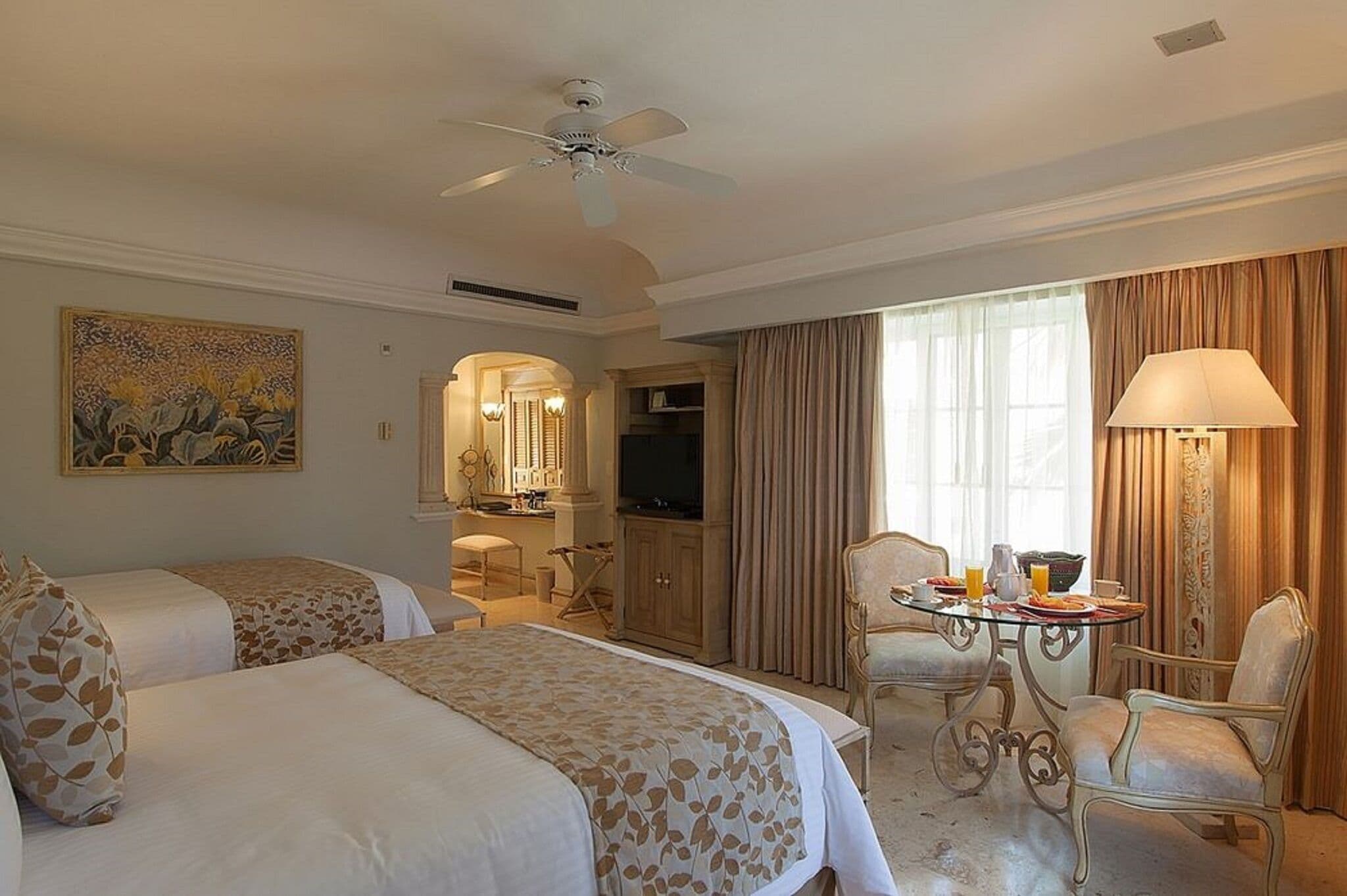 Une chambre d’hôtel avec deux lits, un coin repas comprenant une table et des chaises, un téléviseur et un ventilateur de plafond.