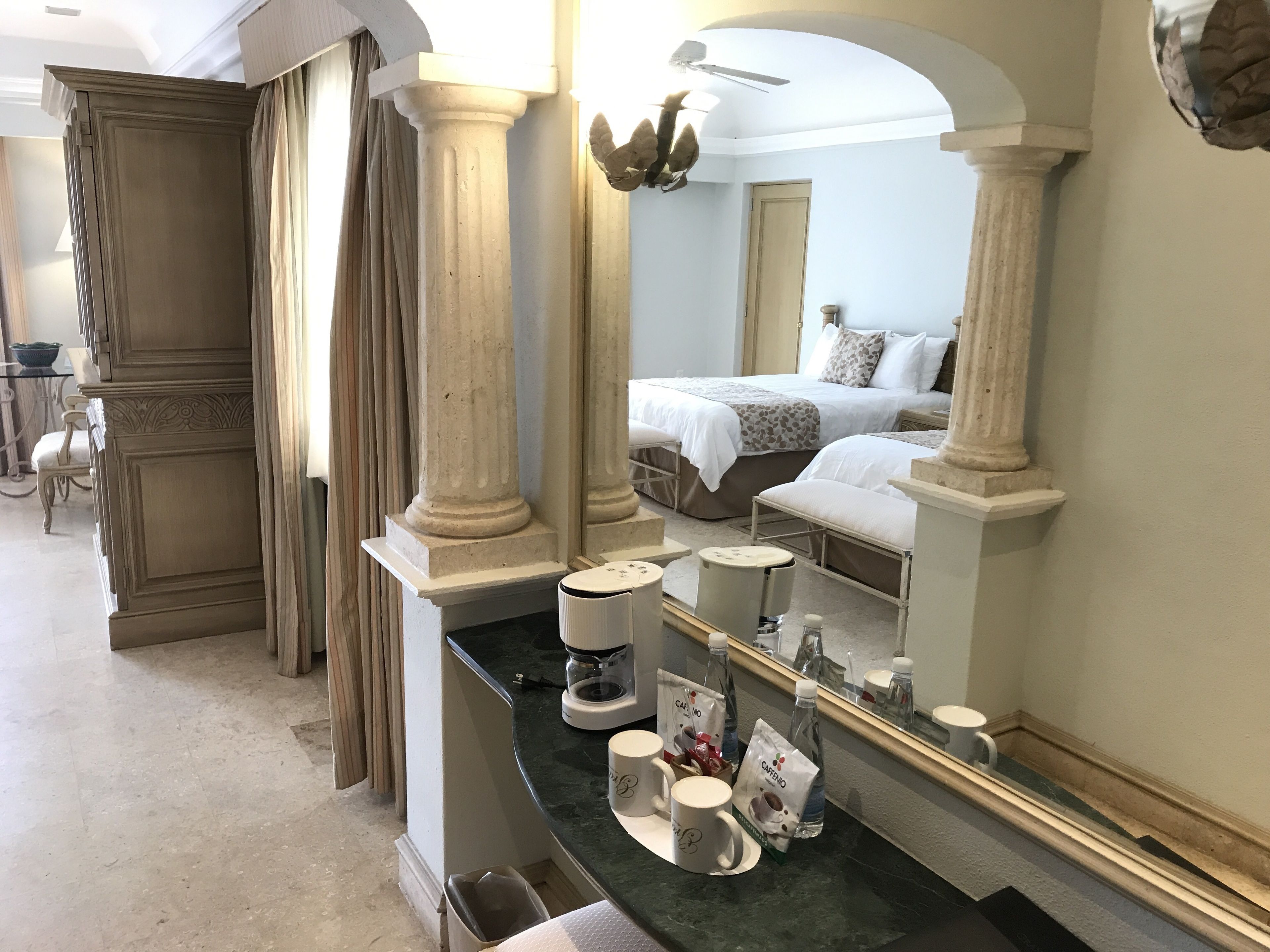A hotel room with a large bed, a sitting area with a chair, a coffee machine, and a counter with a mirror.