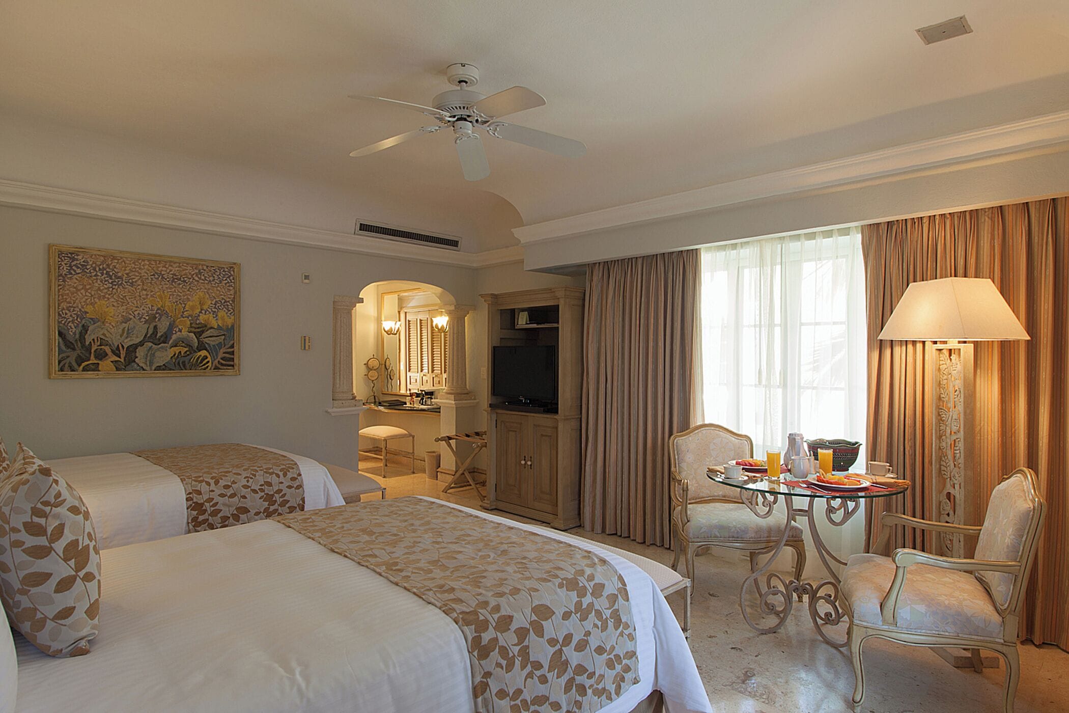 Une chambre d’hôtel avec deux lits, une télévision, une table à manger avec des chaises et un ventilateur de plafond.