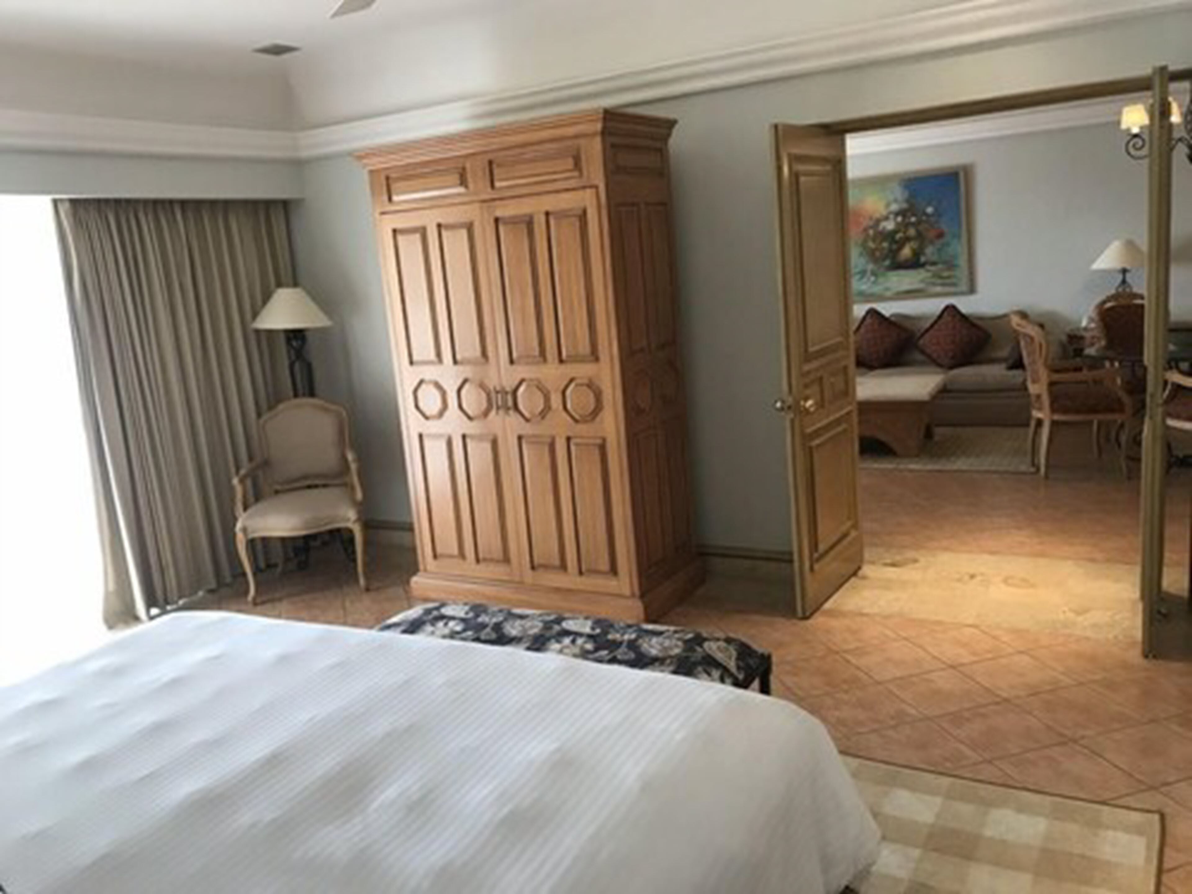 Habitación de hotel con una cama grande, un armario, una zona de estar con sofá y sillones, y un cuadro en la pared.