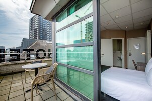 Una habitación de hotel con un ventanal grande, una cama, una mesita y dos sillas.