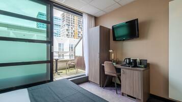 Une chambre d’hôtel comprenant un lit, un bureau avec une chaise, une télévision et une vue sur la ville grâce à une grande fenêtre.