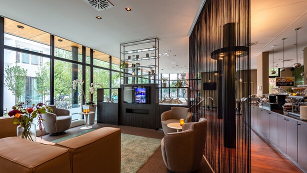 Un moderno vestíbulo de hotel con áreas de estar, un televisor y una cocina a la vista.