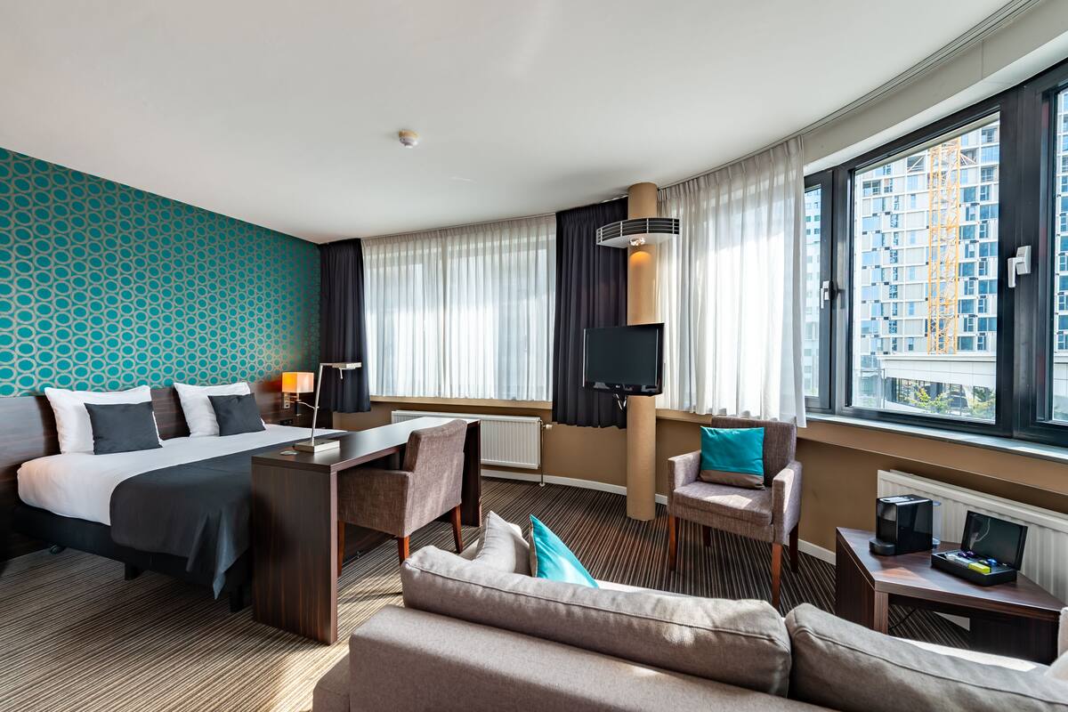 A hotel room with a large bed, a sofa, a desk, and a TV.
