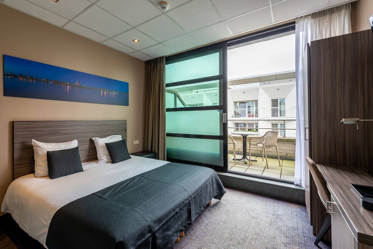 A hotel room with a large bed, a desk, and a balcony with a table and chairs.
