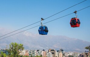 Dos telecabinas, una azul y otra roja, suspendidas sobre una ciudad con montañas al fondo.
