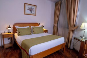 Una cama bien hecha con una colcha y almohadas verdes, una mesita de noche con una lámpara, una silla y un escritorio con una lámpara.