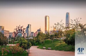 Un parque con una escultura, un sendero y un horizonte urbano al fondo.