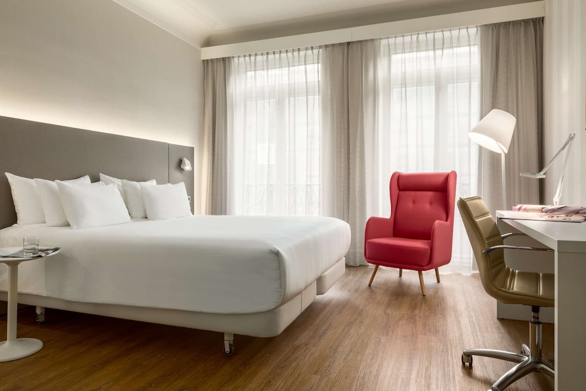 A hotel room with a large bed, a desk with a chair, and a lamp.