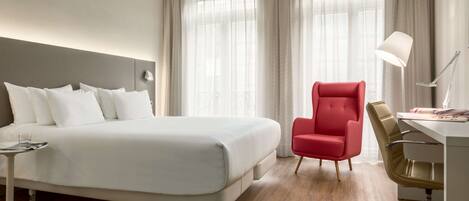 A hotel room with a large bed, a desk with a chair, and a lamp.