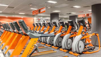 A gym with multiple treadmills lined up in rows, a clock, and a sign indicating a cardio area.
