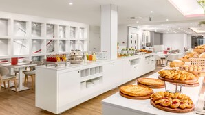 Un vestíbulo moderno de hotel con un mostrador de recepción central, decoración blanca y diversas opciones de comida y bebida.