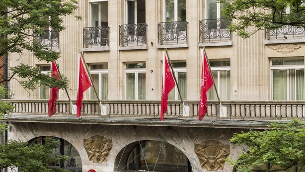 Un hotel con fachada clásica, varios balcones y banderas rojas.