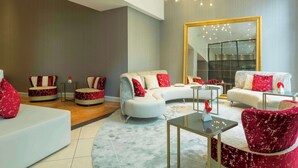 Una sala de estar moderna con un sofá blanco, sillones rojo y blanco, una mesa de centro de vidrio y un espejo grande en la pared.