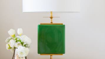 Ein Nachttisch mit einer grün-goldenen Lampe, einer weißen Vase mit Blumen und einer weißen Schublade mit Messingring.