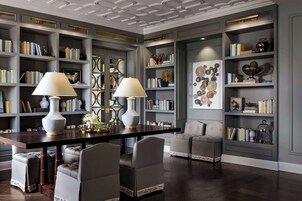 A library with bookshelves, a dining table, and two lamps.