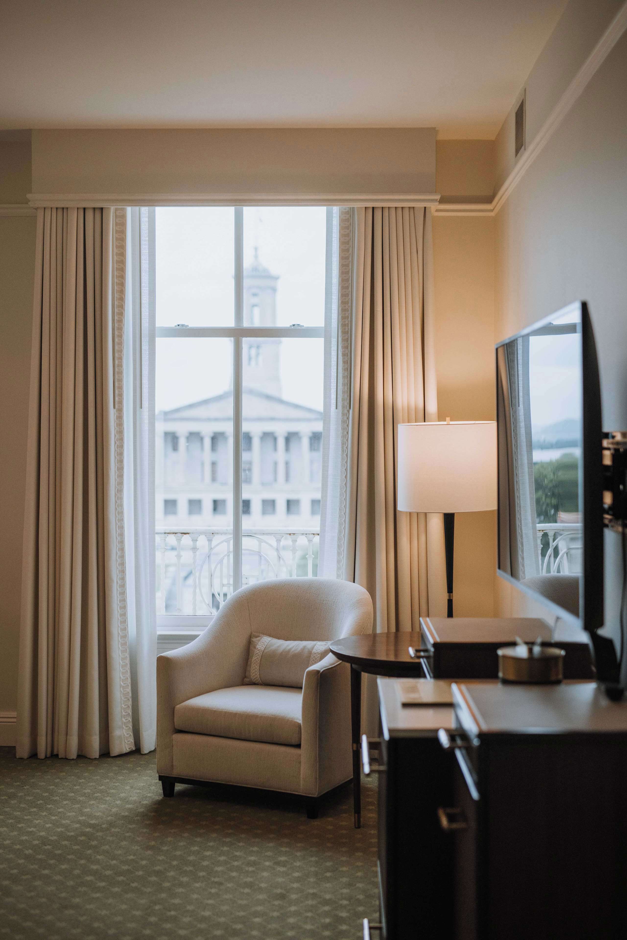 Habitación de hotel con un ventanal grande, un sofá, un escritorio y un televisor.
