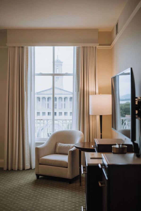 Habitación de hotel con un ventanal grande, un sofá, un escritorio y un televisor.