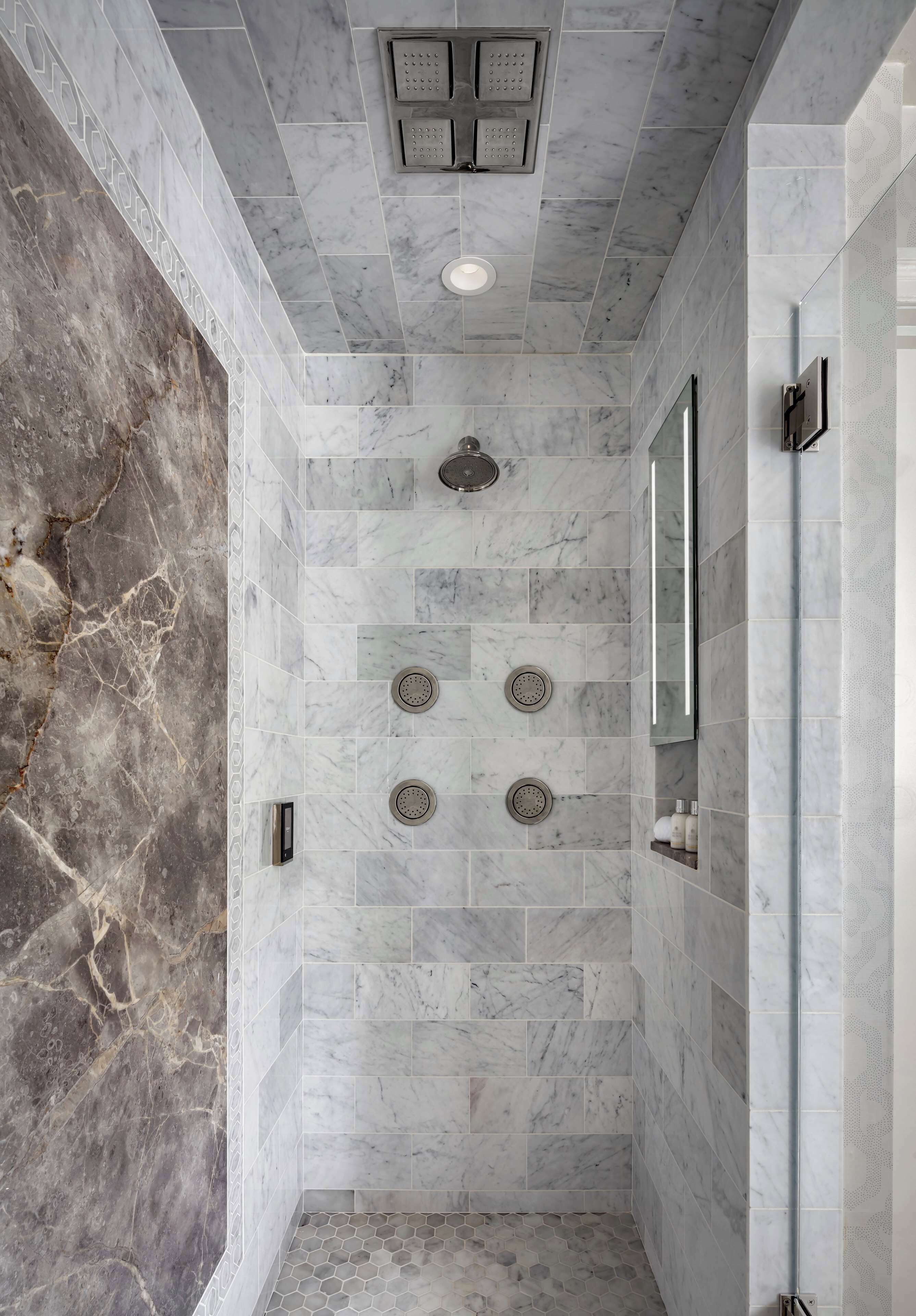 A modern bathroom with marble walls, a shower with multiple nozzles, and a built-in mirror.