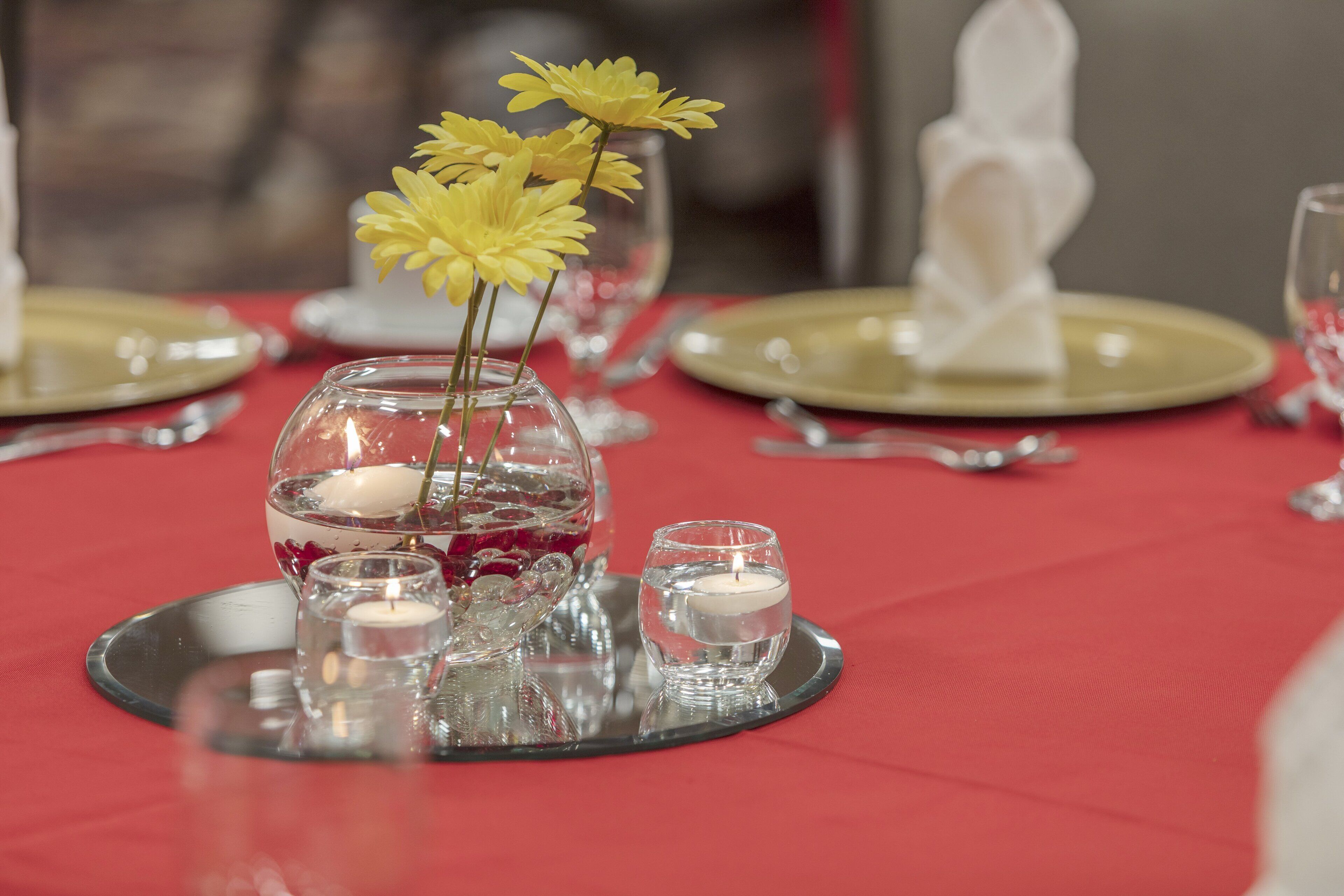 A table set with gold plates, clear glassware, and a centerpiece with yellow flowers and candles.