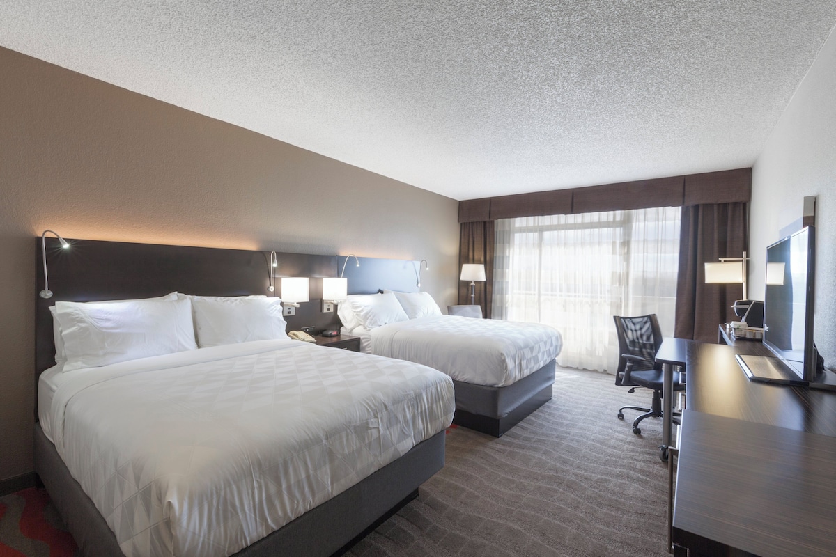 A hotel room with two beds, a desk, a chair, and a television.