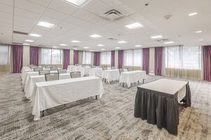 A conference room with multiple tables and chairs, large windows with curtains, and a patterned carpet.