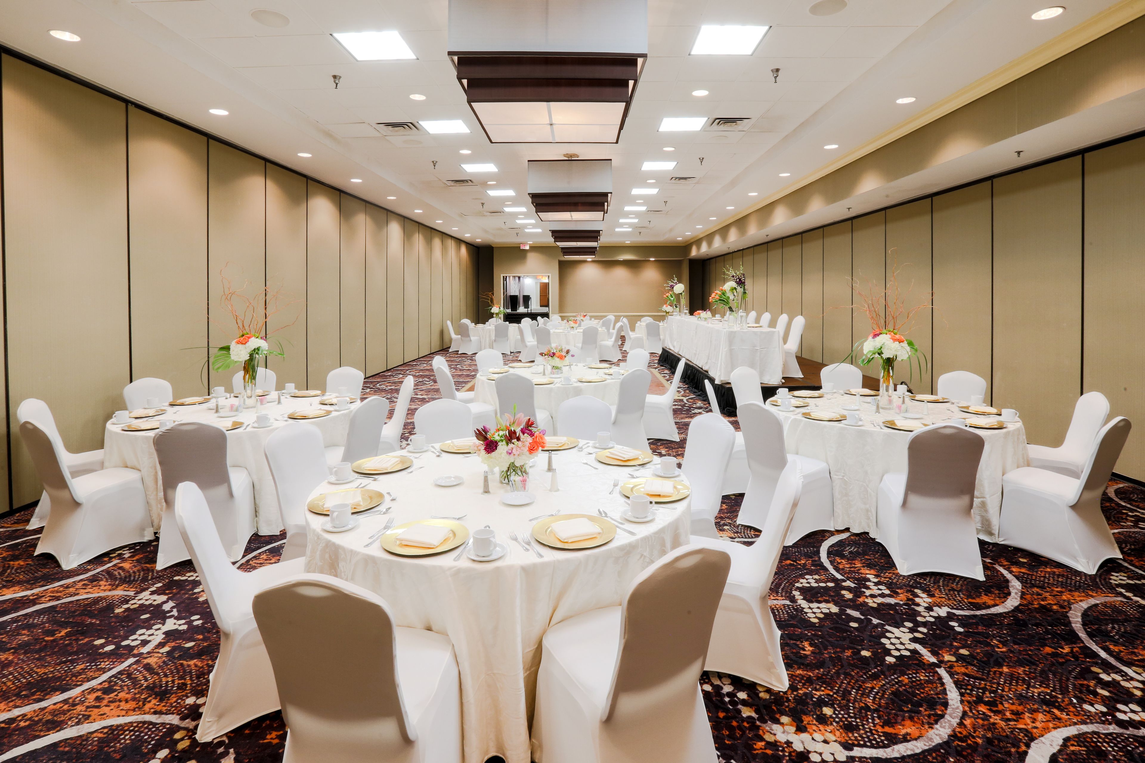 A conference room with round tables, white chairs, and floral centerpieces.