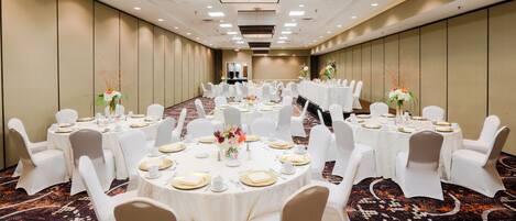 A conference room with round tables, white chairs, and floral centerpieces.