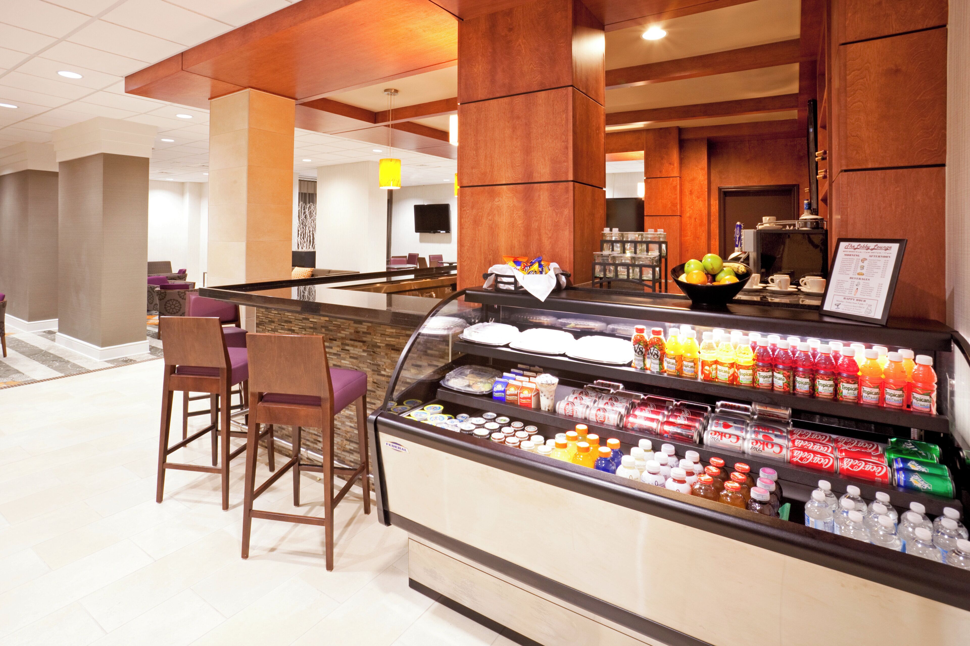 A hotel lobby with a self-service beverage station, seating area, and a reception desk.