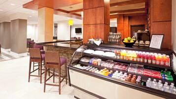A hotel lobby with a self-service beverage station, seating area, and a reception desk.